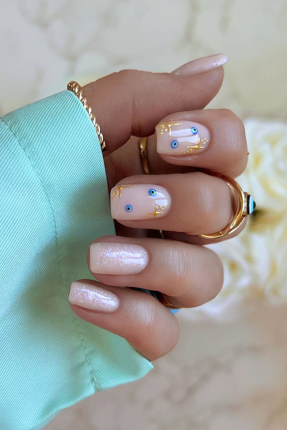 Creamy and glitter beige nails with evil eye and gold starburst details