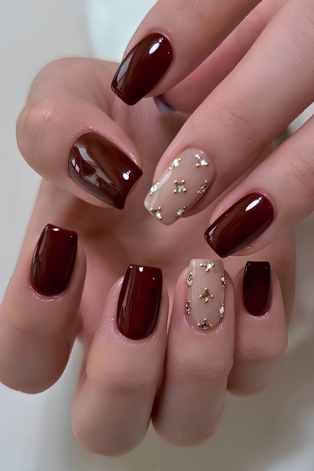 Dark red nails with rhinestones and gold beads