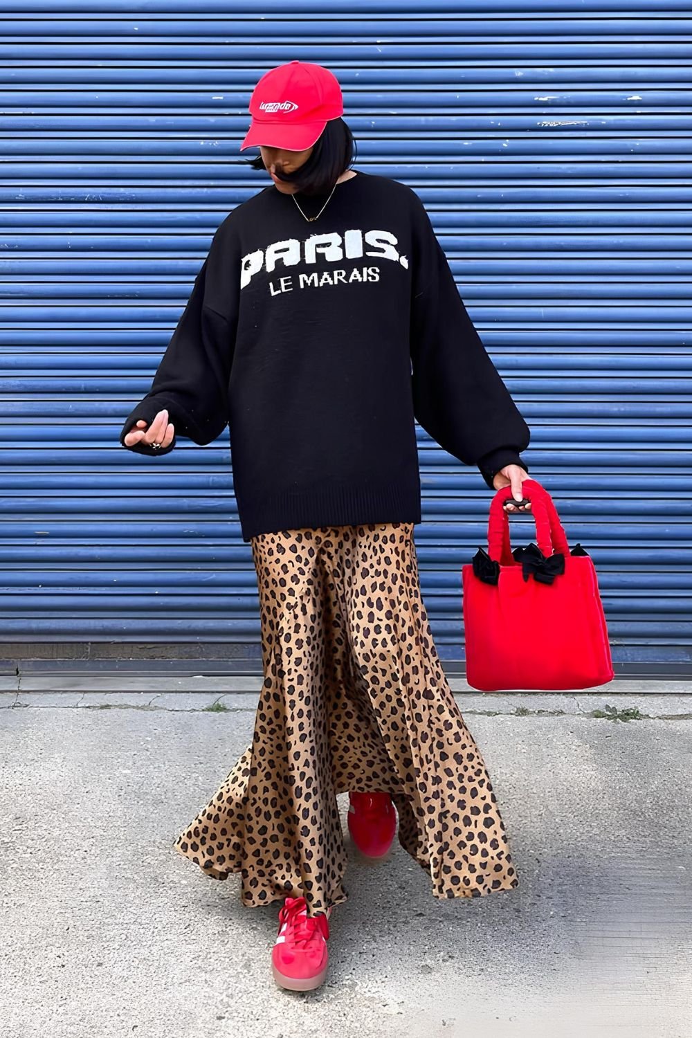 Leopard print silk skirt paired with black oversized hoodie and red hat and sneakers