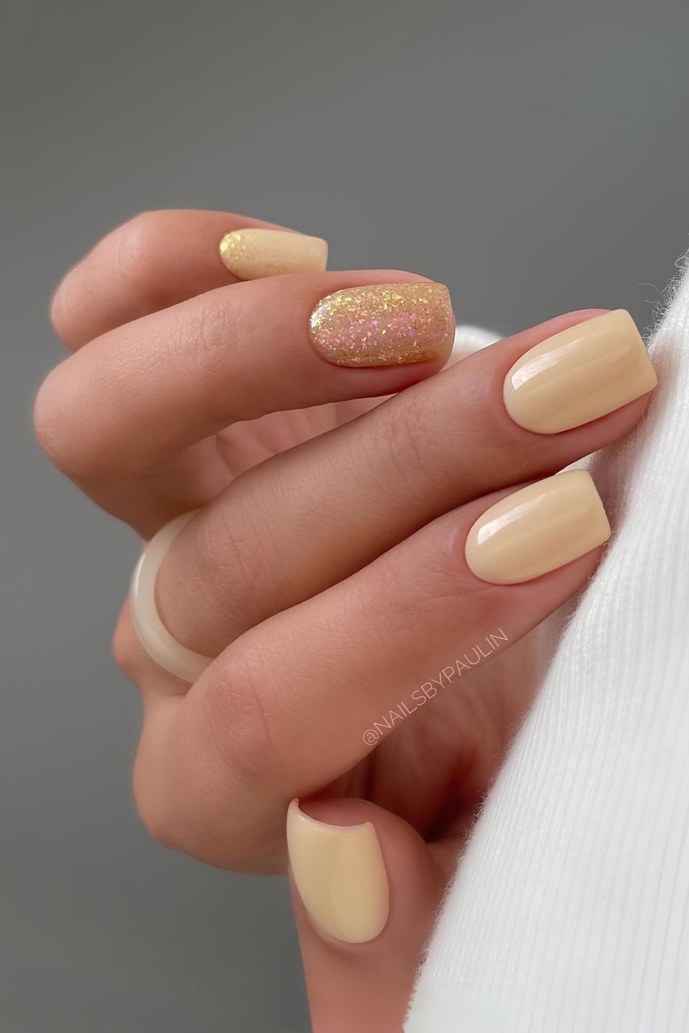 Creamy pale yellow nails with gold glitter accent